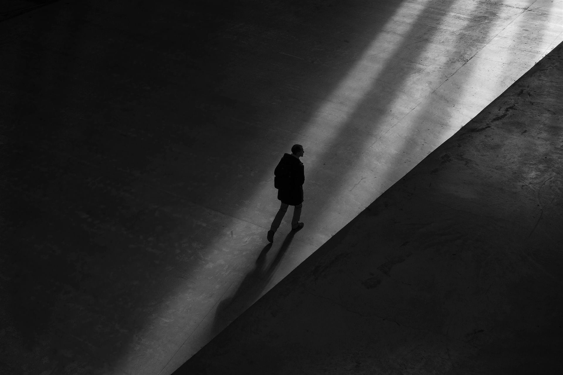 Figura caminando entre luz y sombra sobre concreto, estética monocroma de Hevcaz